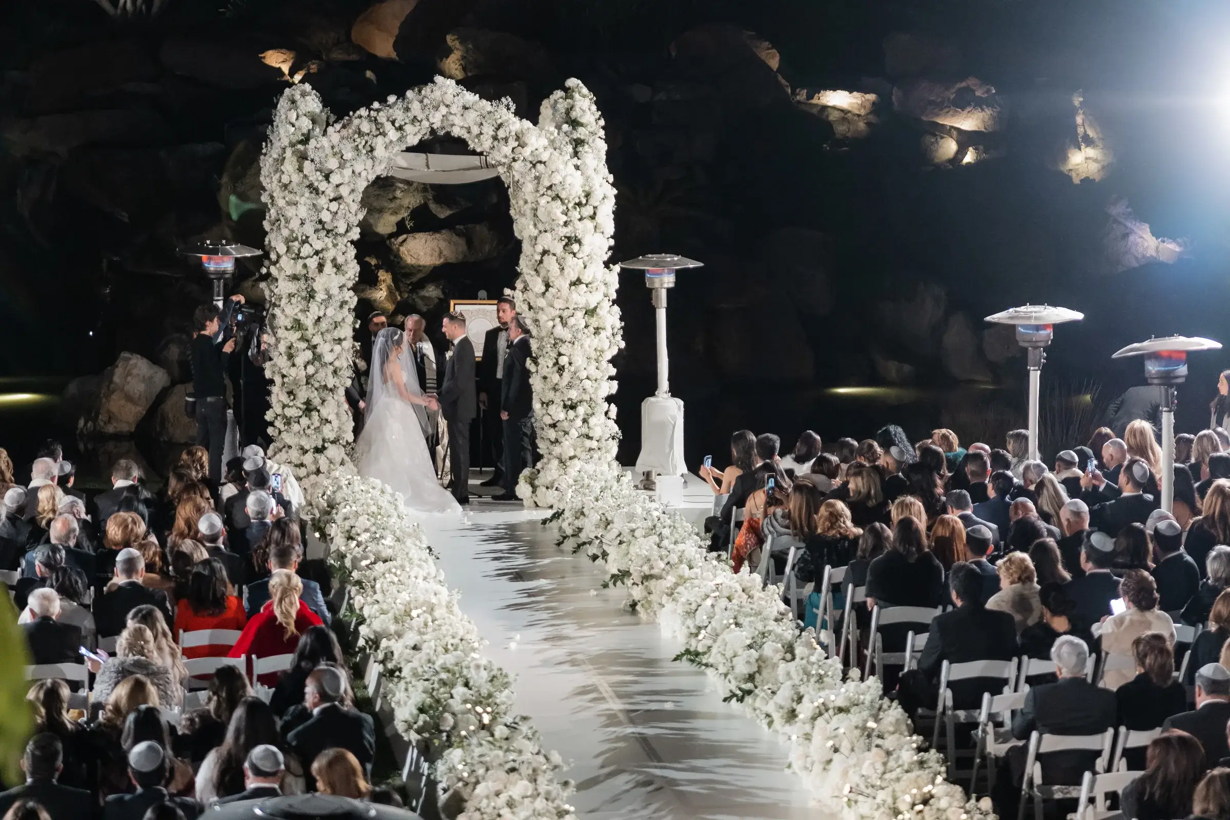 Evening Jewish wedding ceremony under a white floral chuppah with guests at the Four Seasons Hotel Westlake Village