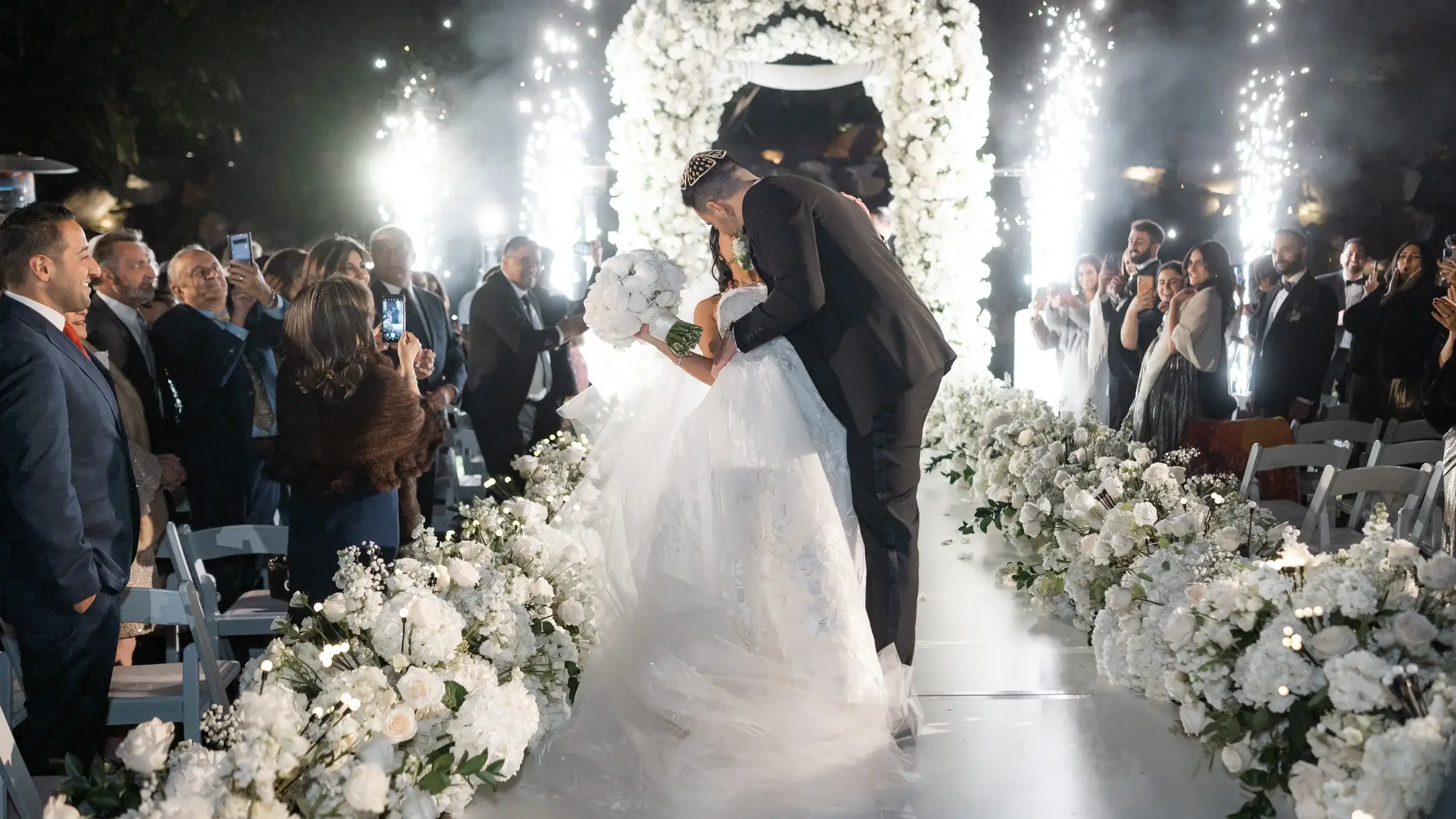Couple kissing at the end of a floral aisle between cold spark fountains at the Four Seasons Hotel Westlake Village