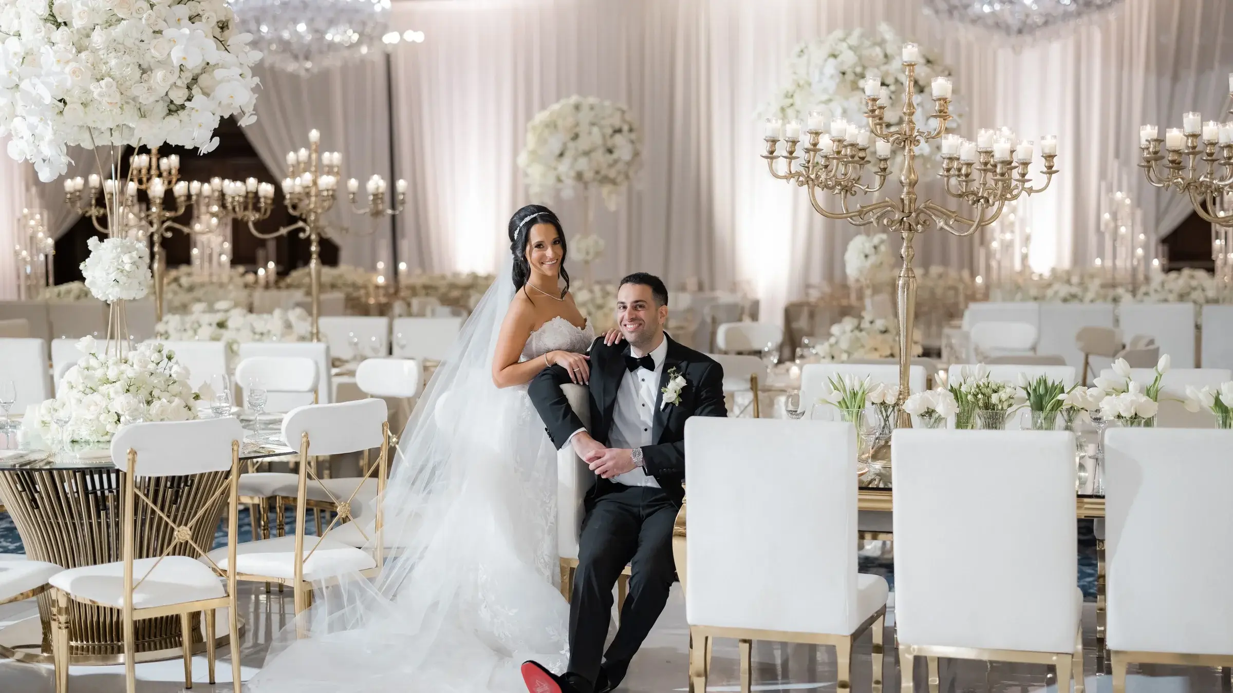 Couple seated among white chairs, gold candelabras and florals in a ballroom at the Four Seasons Hotel Westlake Village