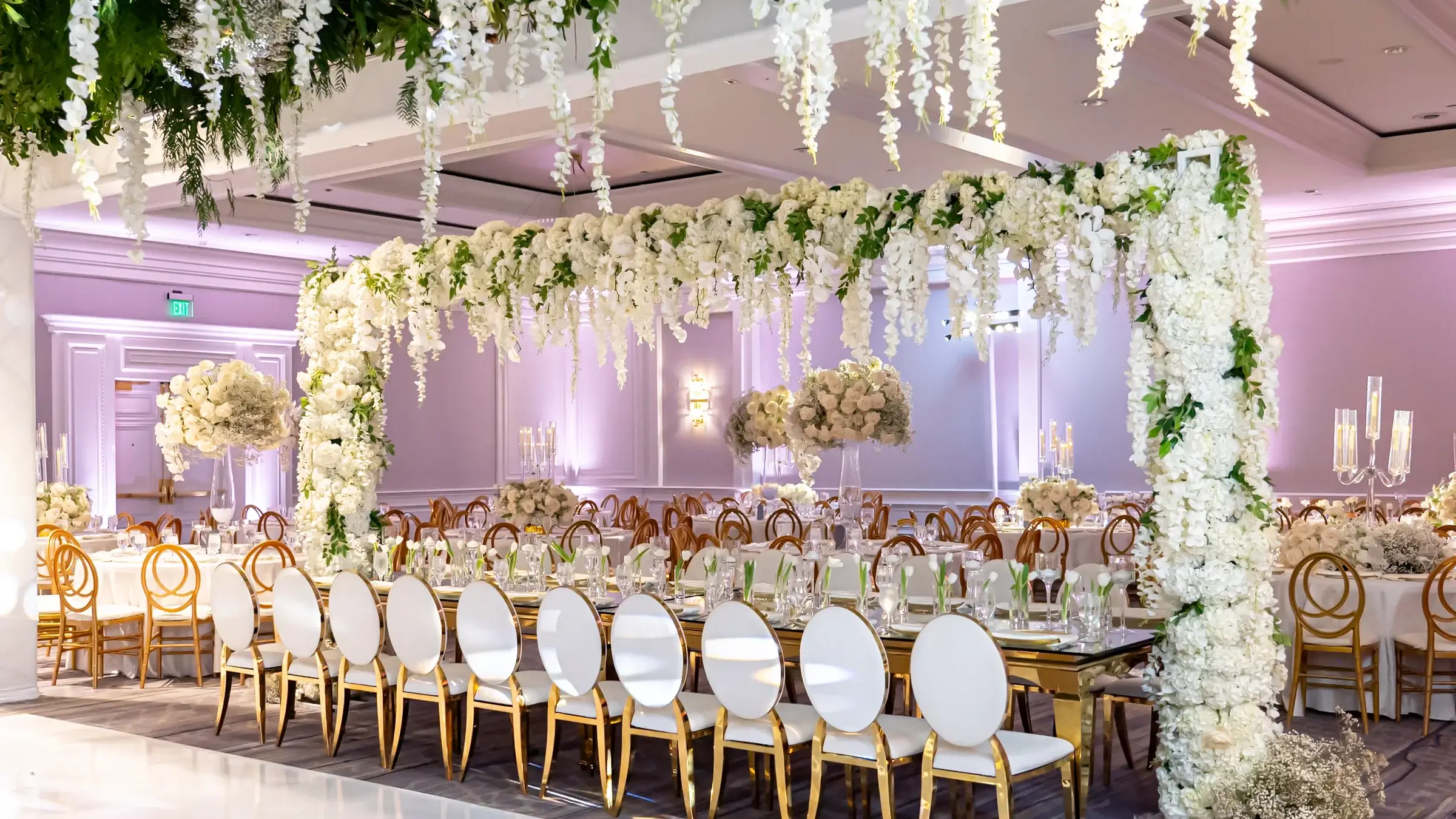 Long gold reception tables under a floral canopy with lavender uplighting at The Ritz-Carlton, Marina del Rey