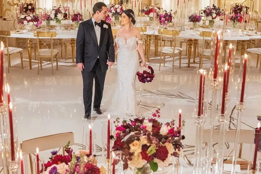 Couple in a ballroom wedding reception set with red florals, tall candles, and warm lighting
