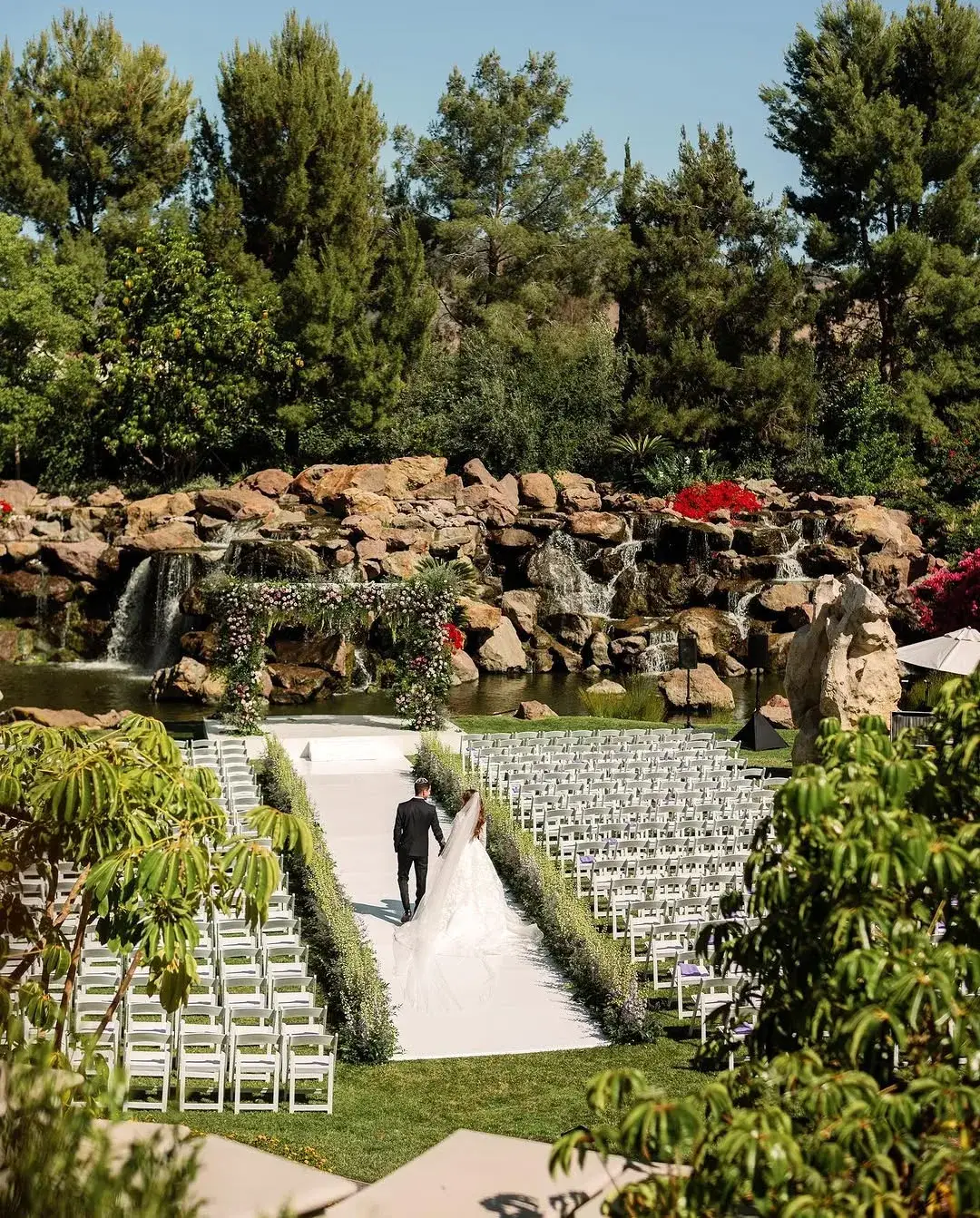 Landscaped grounds with a rock waterfall, mature trees and a garden aisle set for an outdoor gathering in Los Angeles