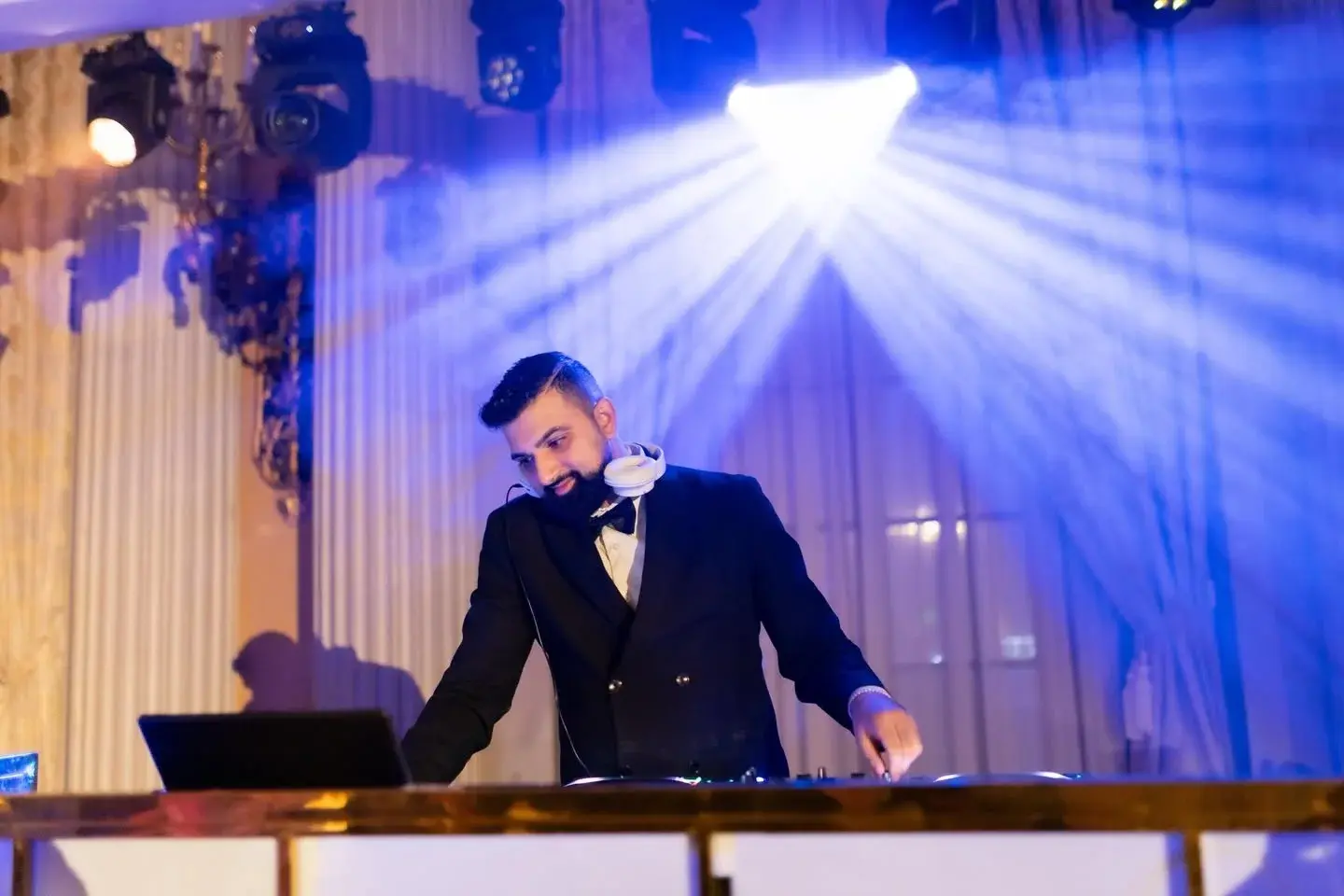 Aryan Rabizadeh (DJ Next Level) performing at the DJ booth in a tuxedo under blue moving-head lighting
