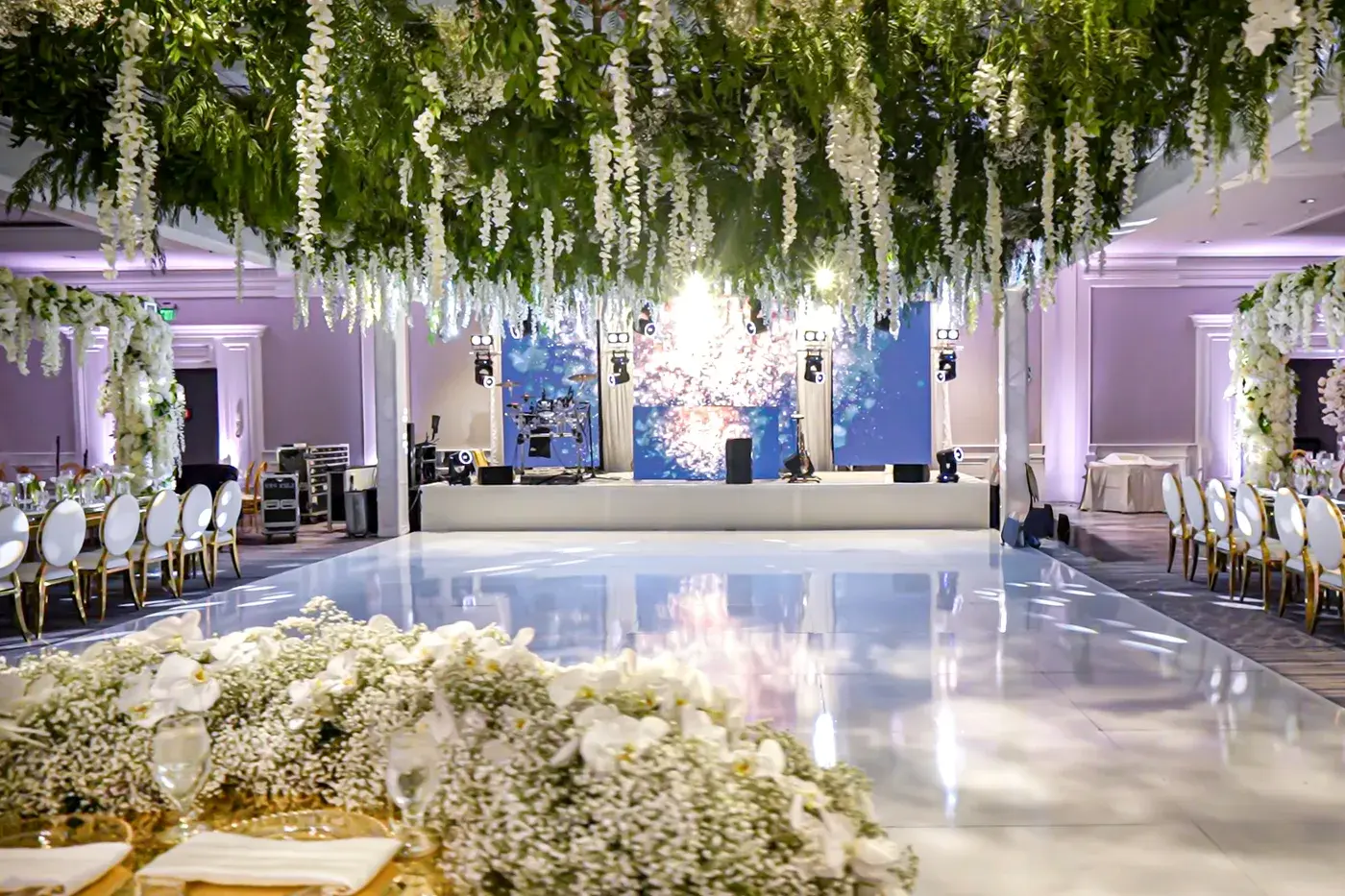 Ballroom set for a wedding with LED video walls behind the stage, a white dance floor and hanging floral ceiling at The Ritz-Carlton, Marina del Rey.