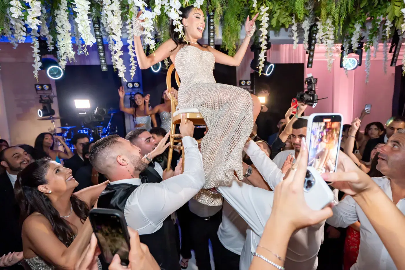 Bride lifted in a chair during the hora under colourful dance-floor lighting and a floral ceiling at The Ritz-Carlton, Marina del Rey.