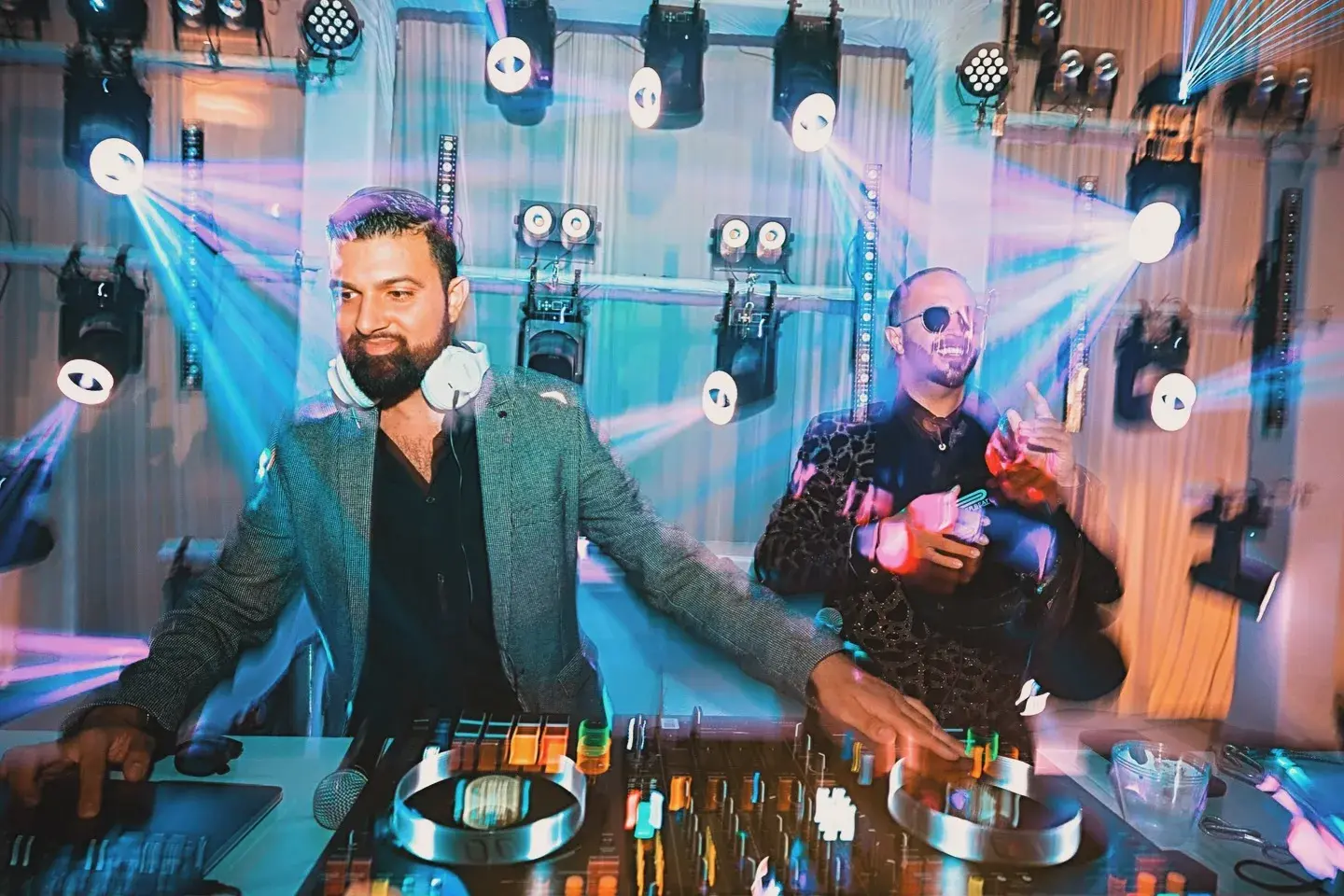 Moving-head fixtures, pixel bars and blinders on truss behind two DJs at a private event
