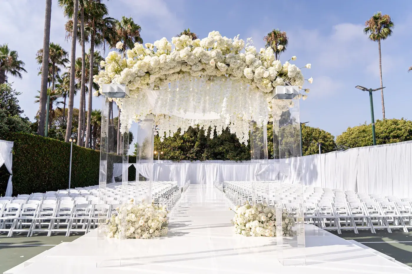 Outdoor event setting with a white floral canopy, staging and palm trees at The Ritz-Carlton, Marina del Rey