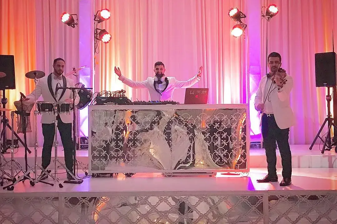 DJ, percussionist and violinist performing on a lit wedding stage with LED fixtures on stands