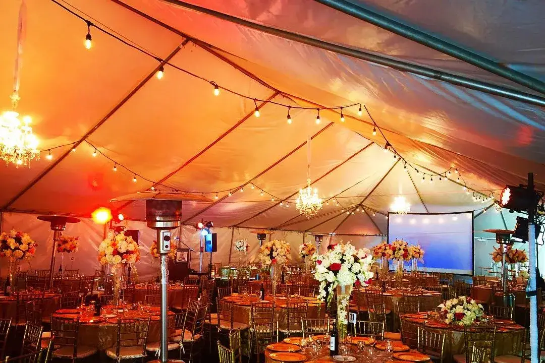 Tented outdoor event with string lights, warm uplighting, and a projection screen