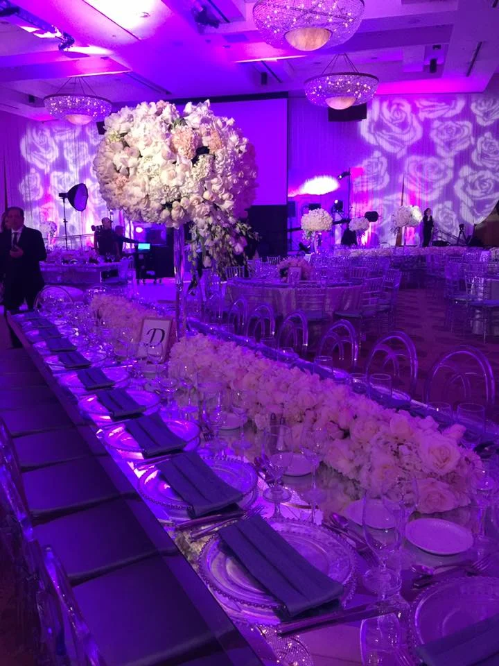 Ballroom at a bat mitzvah at Sinai Temple: white floral centrepieces lit by pin spots, rose-pattern gobos washing the walls and purple uplighting through the room